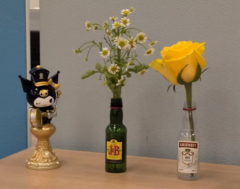 Two flower stems in bottles beside a small figurine on a desk